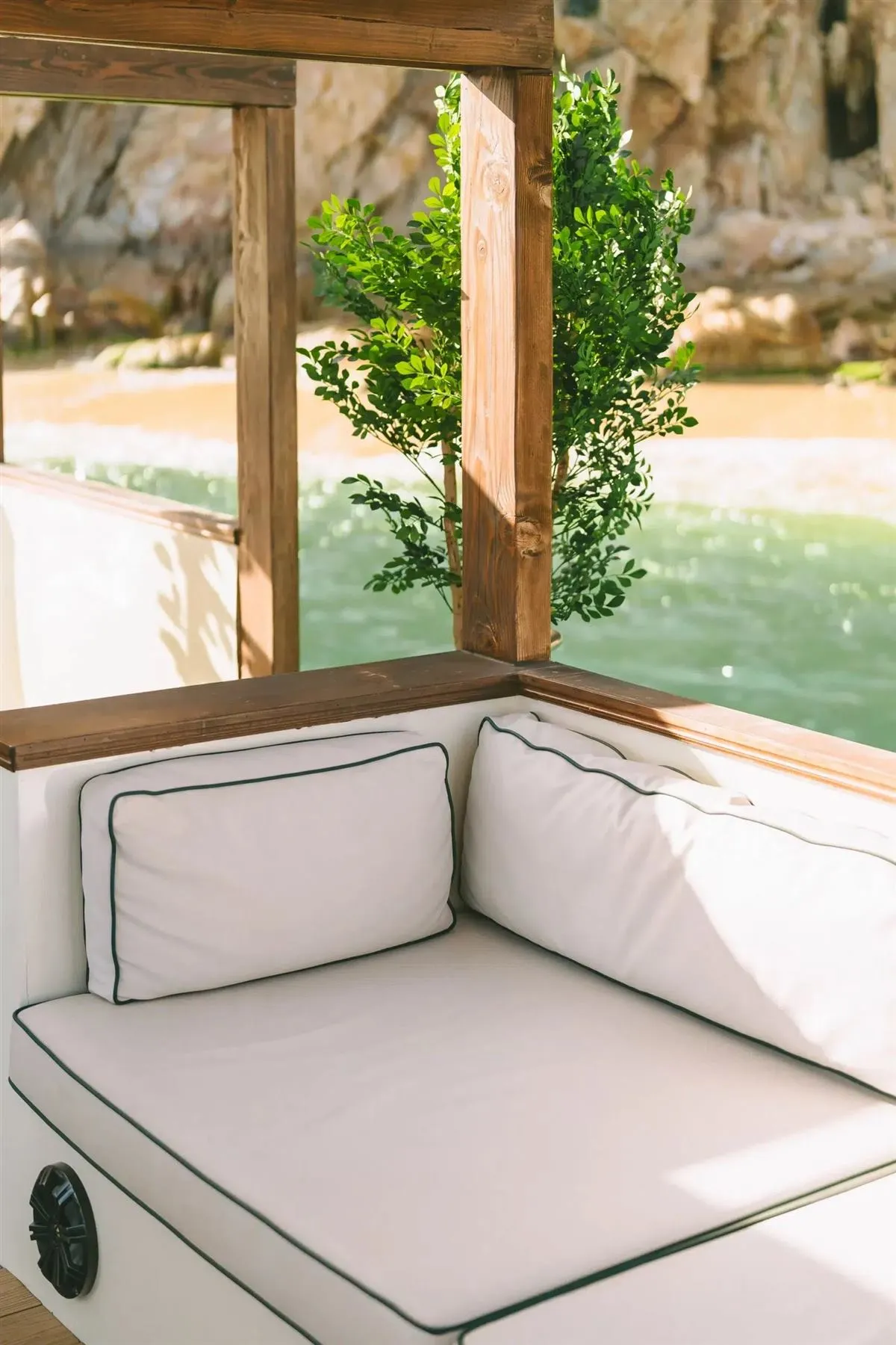 Cushioned seating on the shaded deck of the catamaran with greenery and the water behind