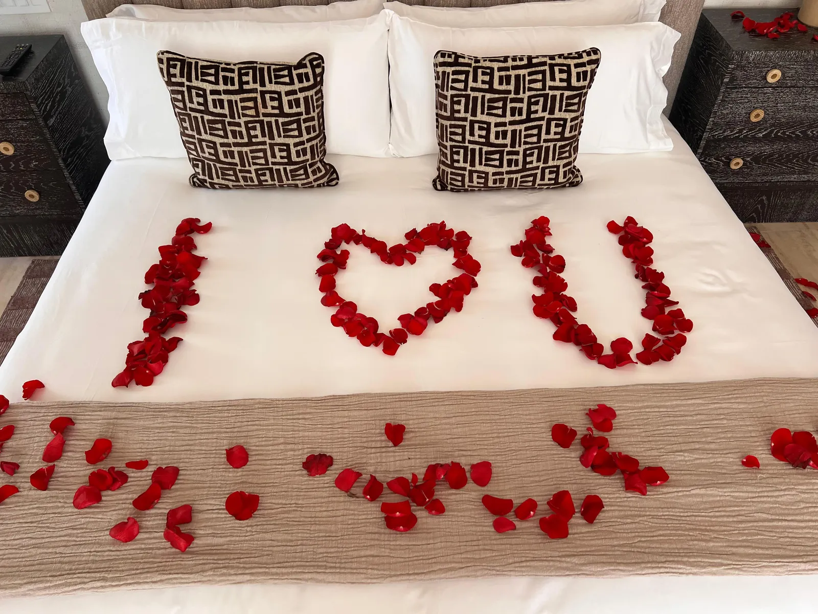 Hotel bed decorated with red rose petals spelling I love you