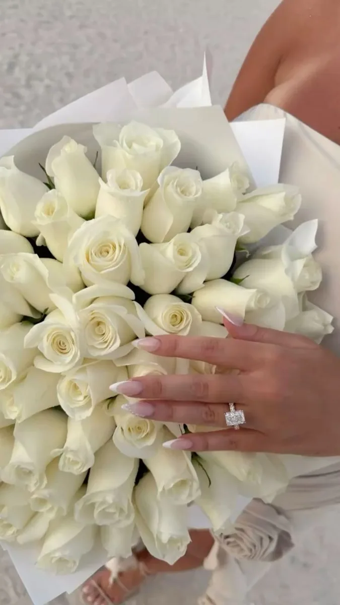 Bouquet of white roses held beside a hand wearing an engagement ring