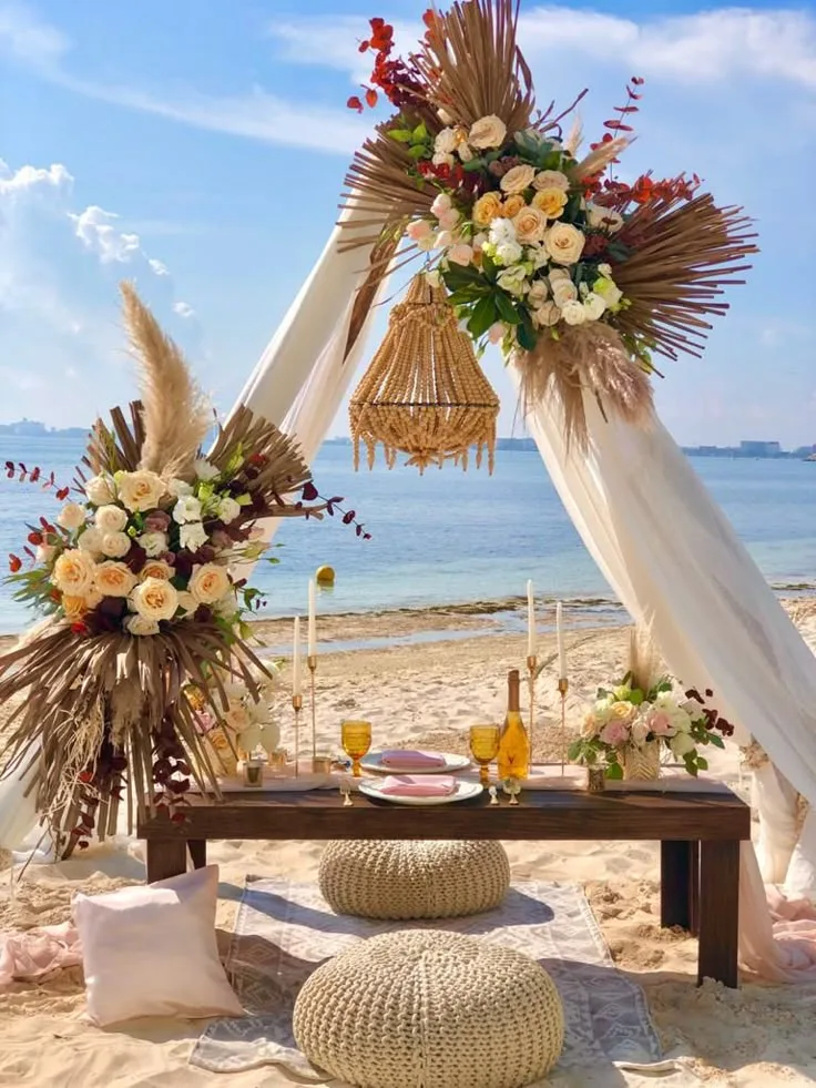 Boho styled dinner table on the sand with pampas grass, florals and floor cushions