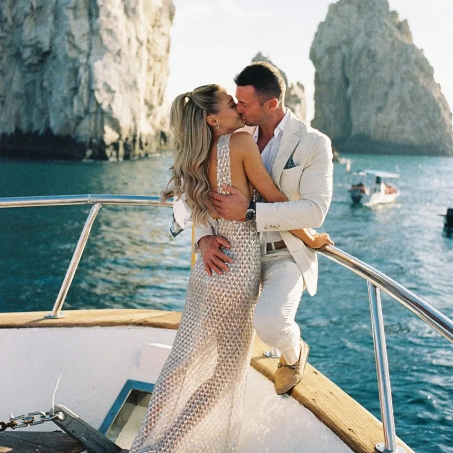 Couple kissing on the bow of the yacht with El Arco behind them