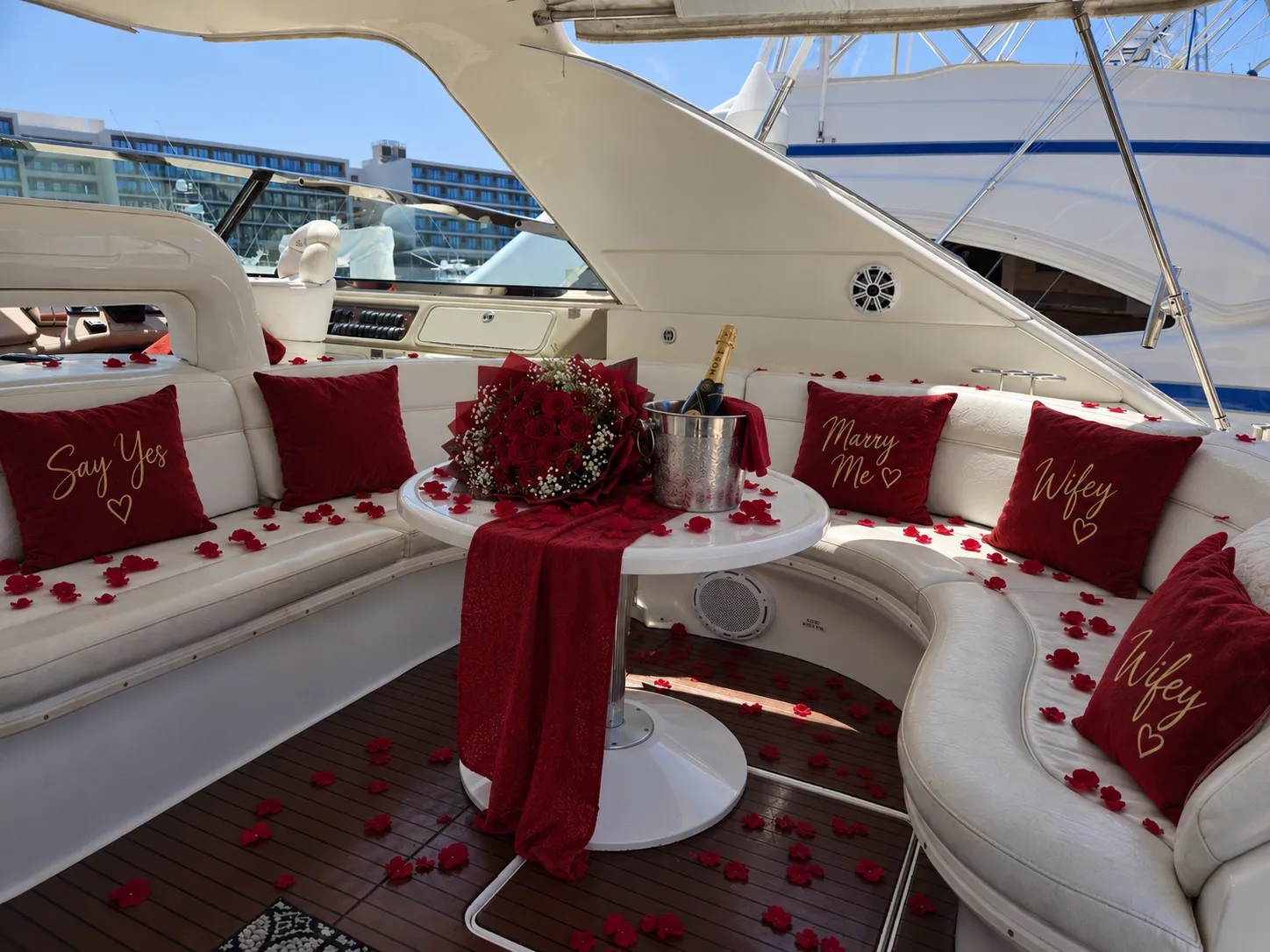 Yacht deck styled with red Say Yes and Marry Me cushions, rose petals, red roses and champagne on ice